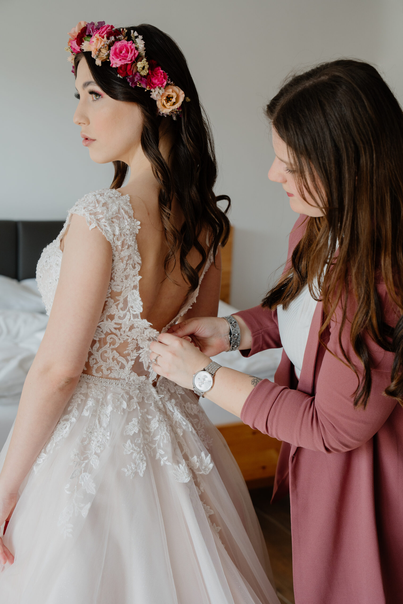 Hochzeitsplaner hilft Braut in ihr Brautkleid und macht am Rücken alle Knöpfe zu, Laura Kohlbacher